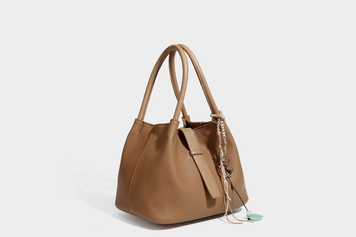 Pebbled leather-look bucket tote bag with rolled double handles, drawstring closure, braided cord charm, and detachable