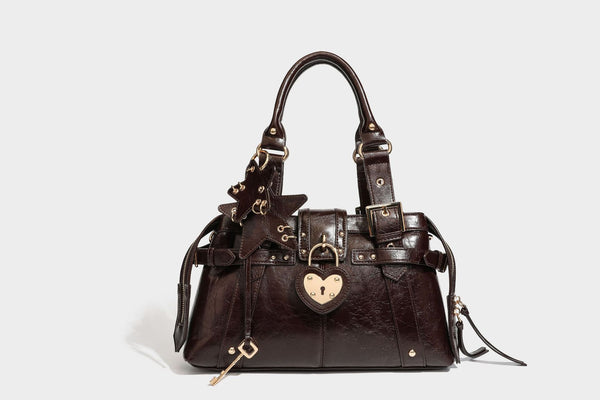 Structured leather-look satchel bag with heart padlock charm, star charm, gold-tone buckle hardware, dual top handles, and