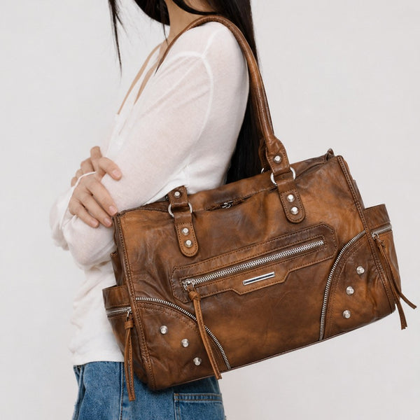 Large distressed leather-look moto tote bag with silver rivets, tassel zip pulls, front zip pocket, and dual top handles