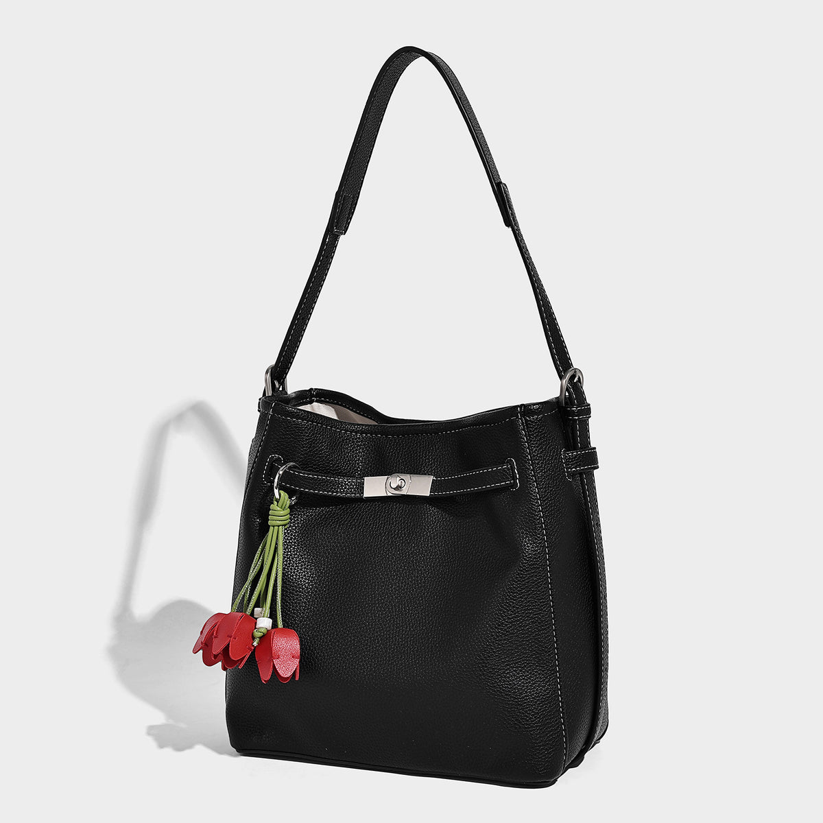 Soft-structured pebbled bucket shoulder bag with front turn-lock strap detail, adjustable strap, and hanging floral tassel