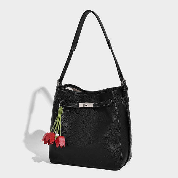 Soft-structured pebbled bucket shoulder bag with front turn-lock strap detail, adjustable strap, and hanging floral tassel