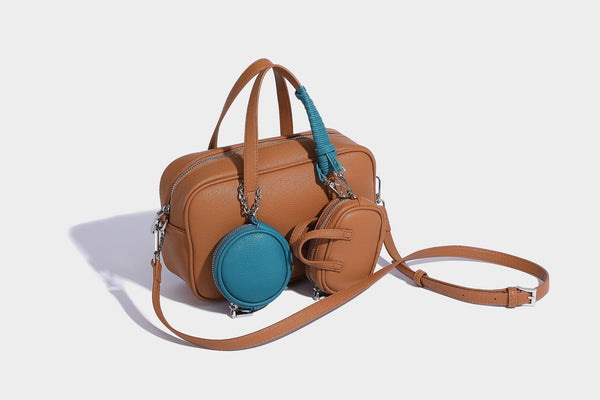 Structured pebbled leather-look Boston bowling bag in tan with blue detachable round mini pouch, dual top handles, and