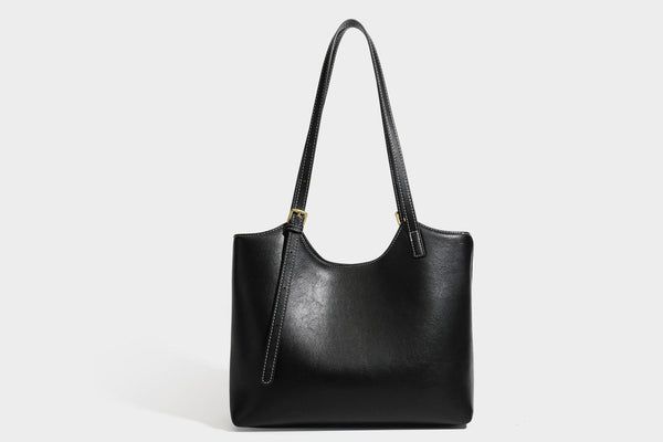 Structured smooth leather-look tote bag with long shoulder strap, gold-tone hardware, and hanging tassel-coin charm, detail