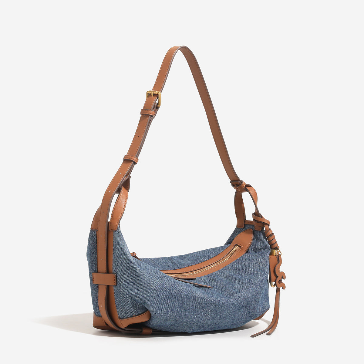 Washed denim canvas crescent hobo bag with tan leather-look trim, knotted strap detail, and gold-tone zipper hardware, detail