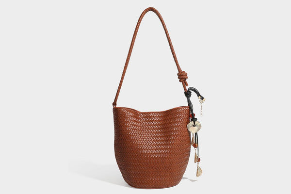 Olive green woven leather-look bucket bag with braided crossbody strap, knotted adjustment, and gold-tone tassel charm with