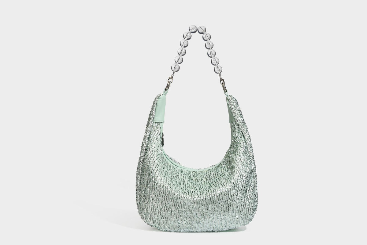 Kleine sichelförmige Schultertasche mit vollständig mit silberfarbenen Pailletten besetzter Außenseite, transparentem Henkel aus kugelförmigen Perlen und Reißverschluss in Silberoptik