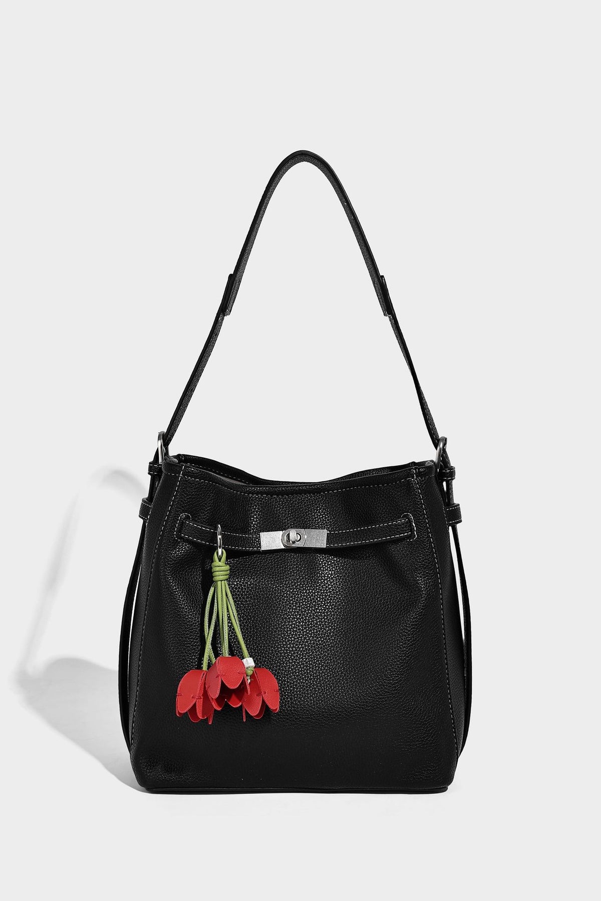Soft-structured pebbled bucket shoulder bag with front turn-lock strap detail, adjustable strap, and hanging floral tassel