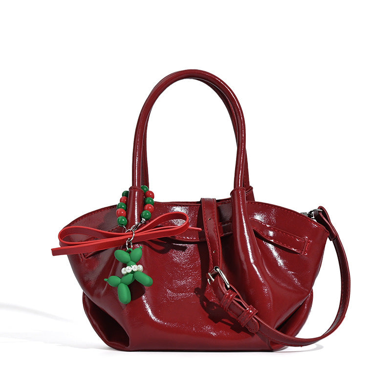 Small structured red glossy PU handbag with bow-and-bead charm, dual top handles, and detachable crossbody strap, detail view
