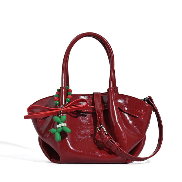 Small structured red glossy PU handbag with bow-and-bead charm, dual top handles, and detachable crossbody strap, detail view