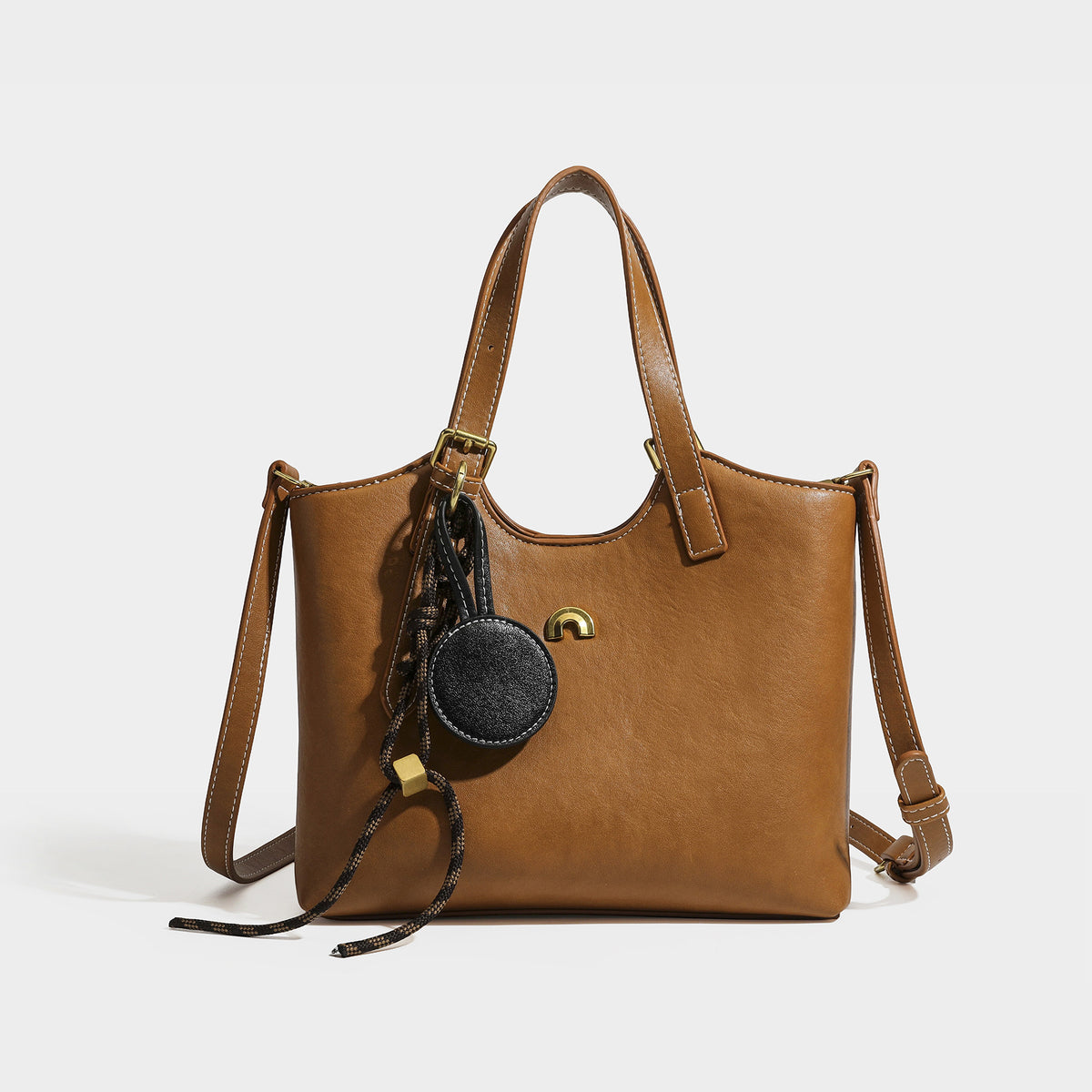 Structured smooth leather-look tote bag with long shoulder strap, gold-tone hardware, and hanging tassel-coin charm, detail