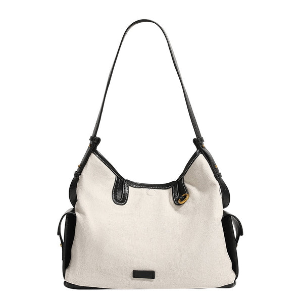 Off-white canvas shoulder bag with black leather-look trim, gold-tone ring hardware, top zip closure, side flap pocket, and