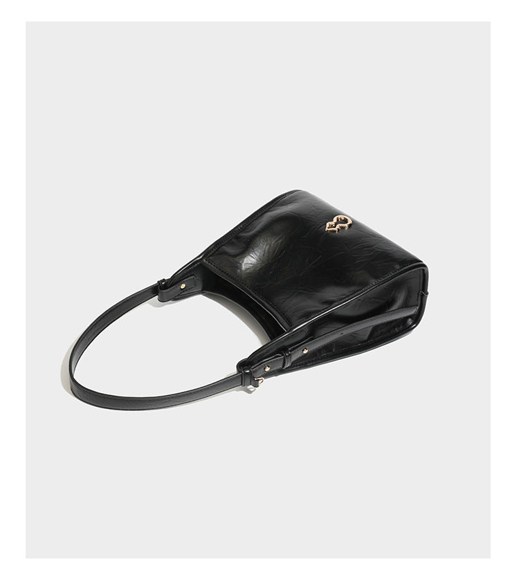 Strukturierte, trapezförmige Schultertasche aus glänzender, geknautscht wirkender Lederoptik mit goldfarbenen Beschlägen auf der Vorderseite und langem, verstellbarem