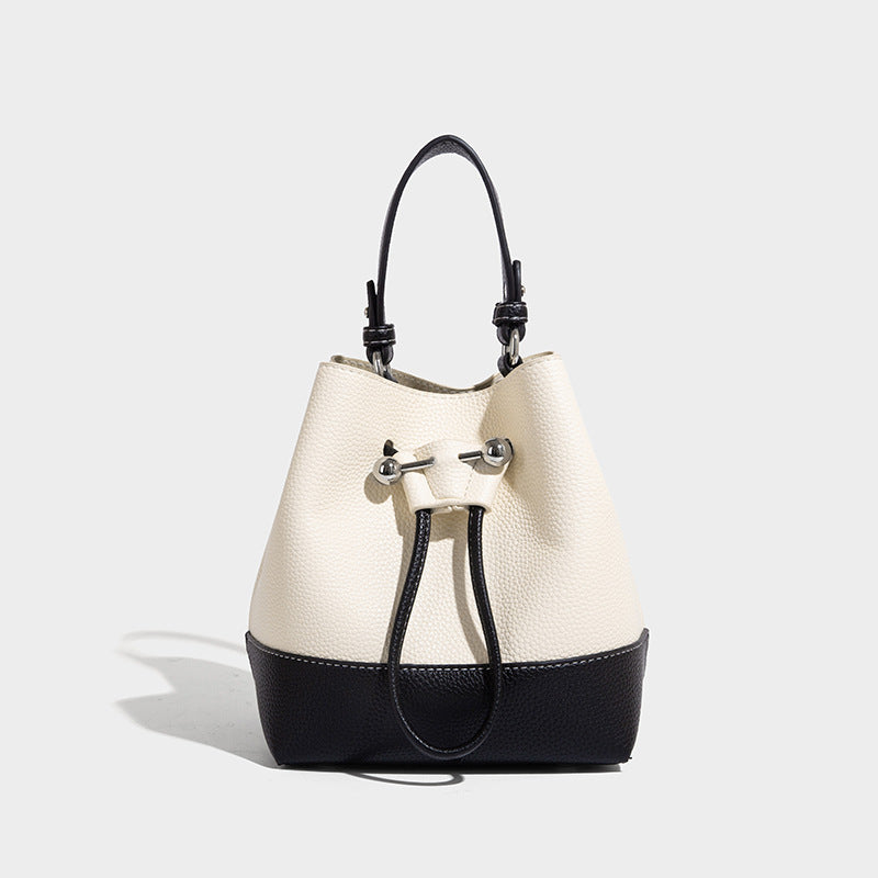 Small two-tone pebbled drawstring bucket bag with tan contrast base, metal toggle hardware, short top handle, and detachable