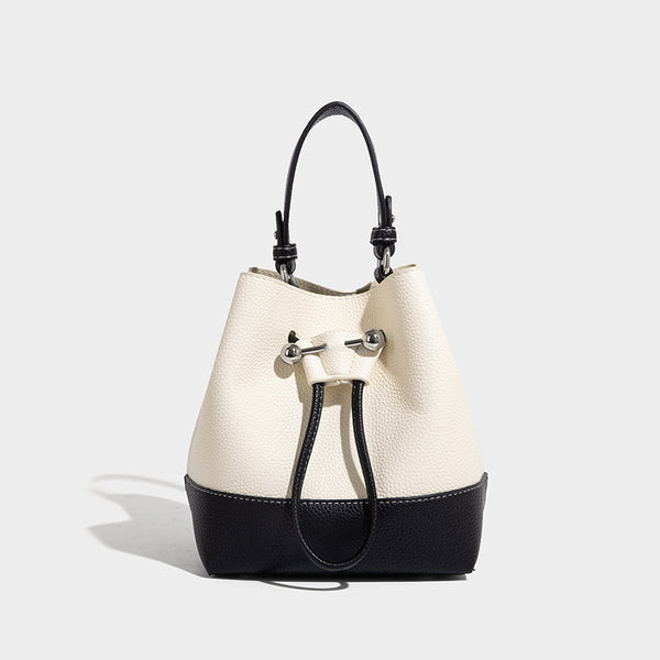 Small two-tone pebbled drawstring bucket bag with tan contrast base, metal toggle hardware, short top handle, and detachable