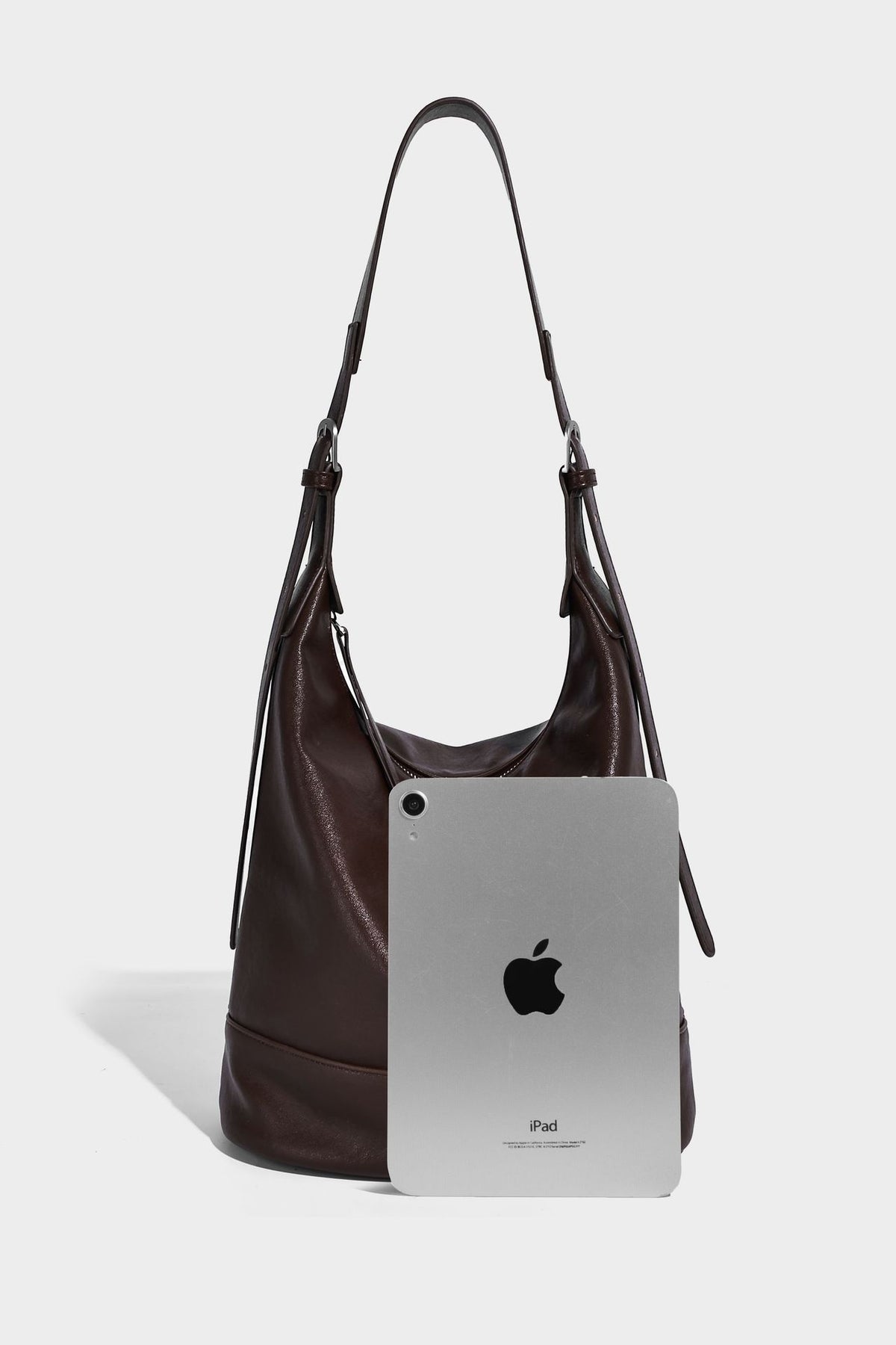 Slouchy bucket hobo shoulder bag in dark brown with glossy leather-look finish, top zip closure, and long adjustable, detail