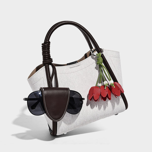 Structured canvas tote bag with knotted top handles, leather-look black trim, front flap pocket, and pink tulip flower charm