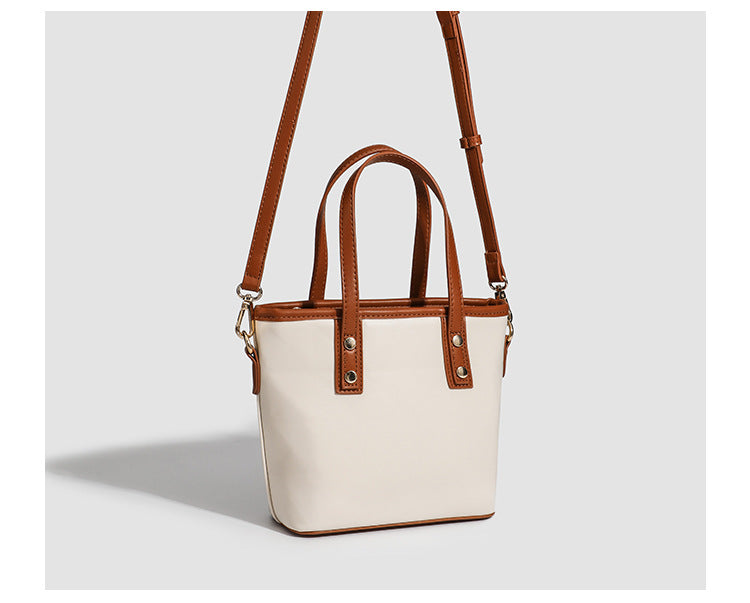 Kleine, formstabile Tote-Tasche mit Henkeln und Besatz in brauner Lederoptik auf einem cremefarbenen Korpus, Reißverschluss oben, goldfarbenen Nieten und