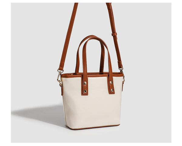 Kleine, formstabile Tote-Tasche mit Henkeln und Besatz in brauner Lederoptik auf einem cremefarbenen Korpus, Reißverschluss oben, goldfarbenen Nieten und