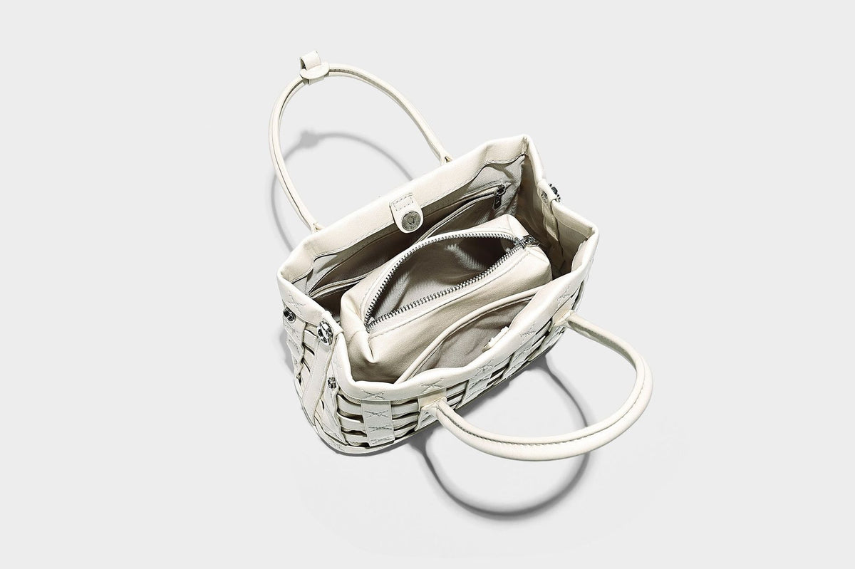 Small structured woven satchel tote with rounded top handles, silver-tone ring hardware, and bead tassel charm, detail view