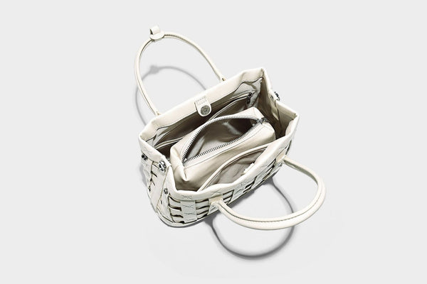 Small structured woven satchel tote with rounded top handles, silver-tone ring hardware, and bead tassel charm, detail view