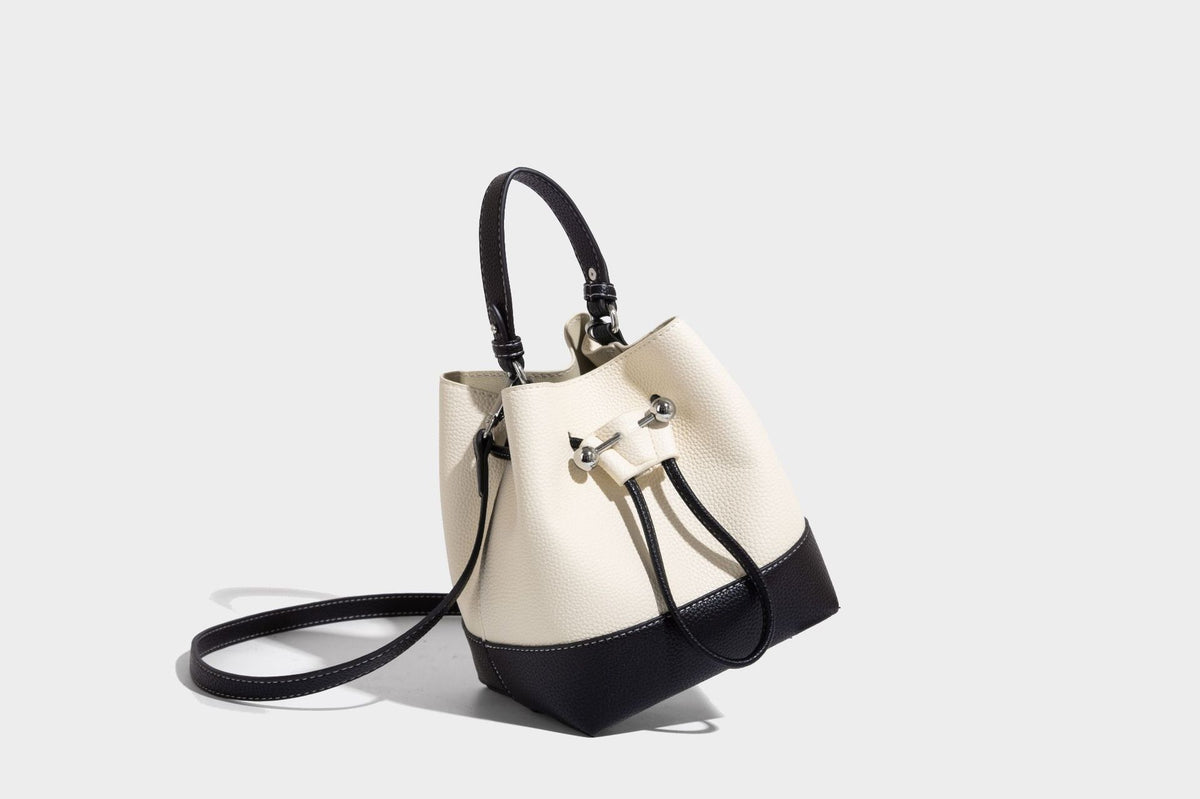 Small two-tone pebbled drawstring bucket bag with tan contrast base, metal toggle hardware, short top handle, and detachable