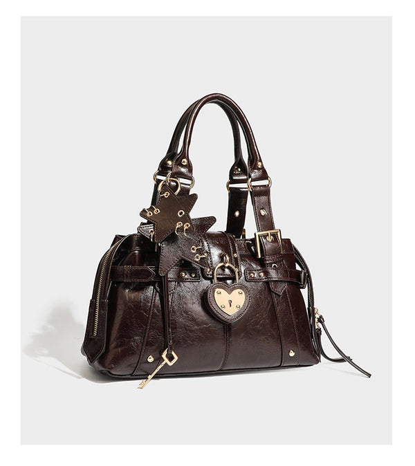 Structured leather-look satchel bag with heart padlock charm, star charm, gold-tone buckle hardware, dual top handles, and