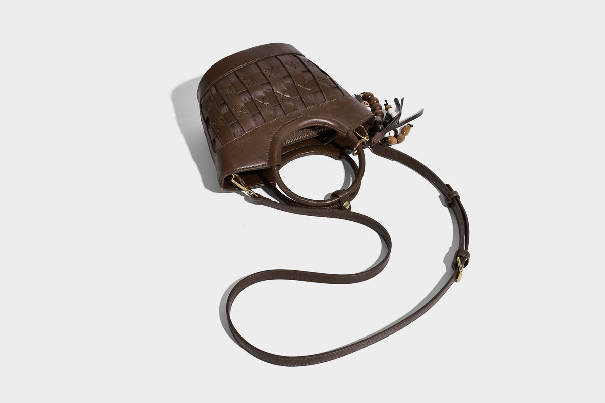 Small woven-panel bucket bag with circular ring handles, beaded tassel charm, and detachable crossbody strap in brown, detail