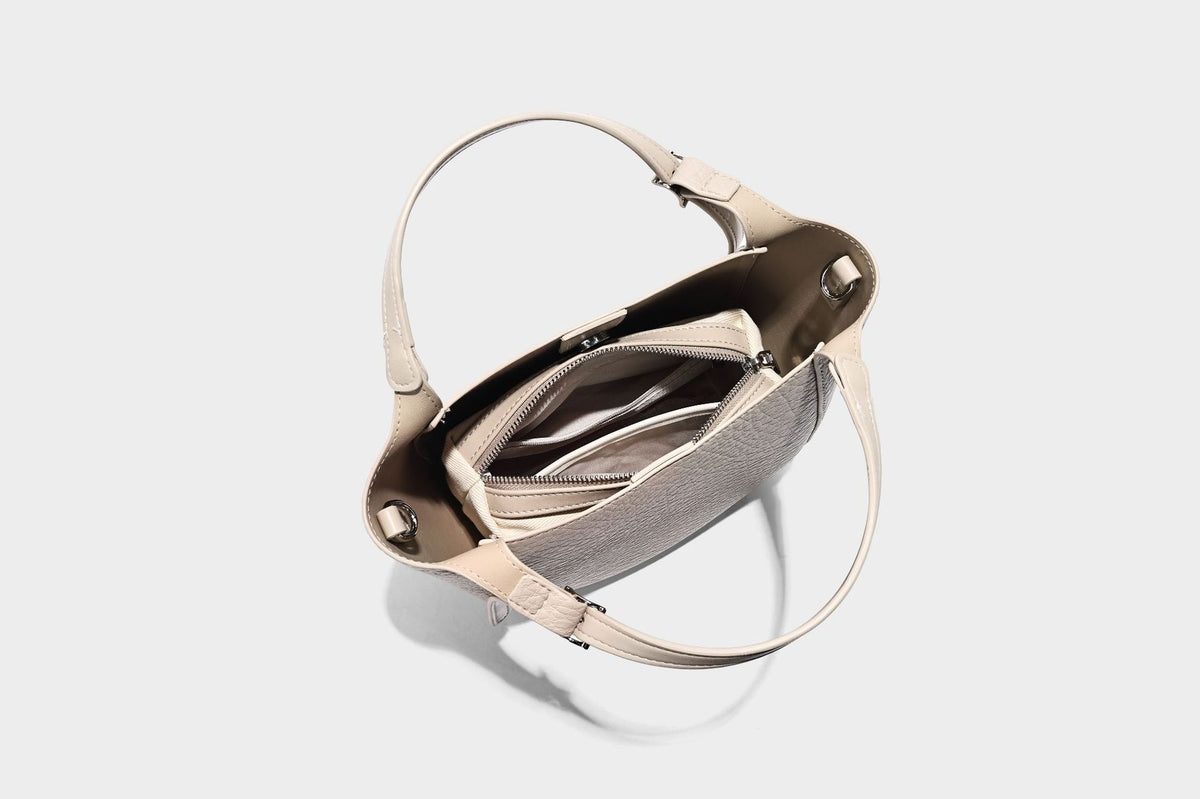 Small pebbled half-moon shoulder bag with dual top handles, detachable crossbody strap, and silver-tone hardware, detail view