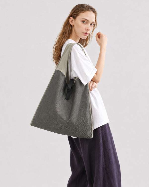 Oversized triangular mesh tote bag with matte olive-khaki fabric straps and trim, dark open-weave mesh body, matte black