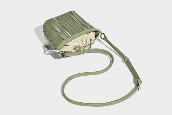 Small woven bucket bag with drawstring top, braided handle, detachable crossbody strap, and silver-tone ring hardware, detail