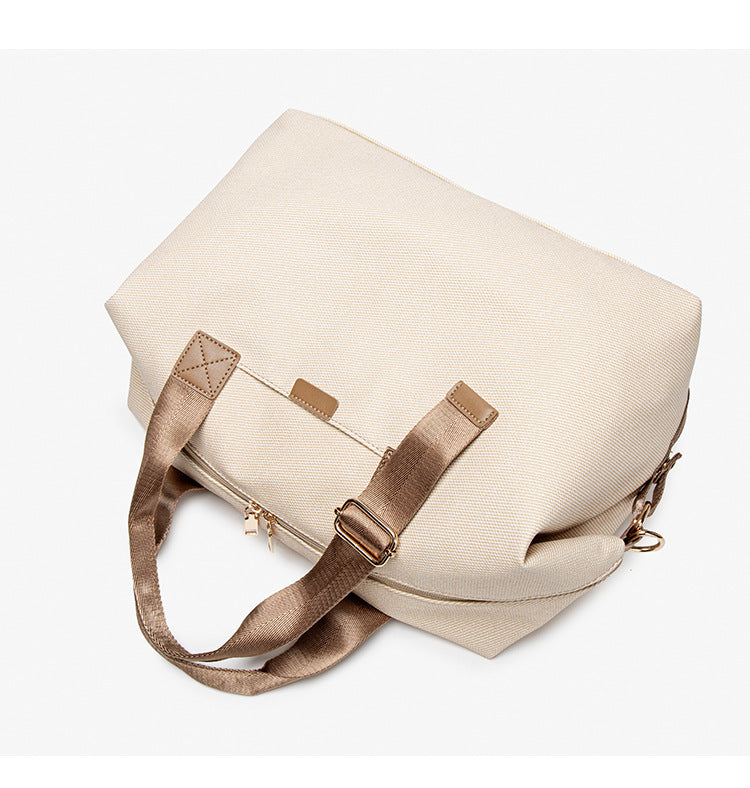 Structured woven duffel bag with dual tan webbing handles, detachable shoulder strap, top zip closure, and gold-tone