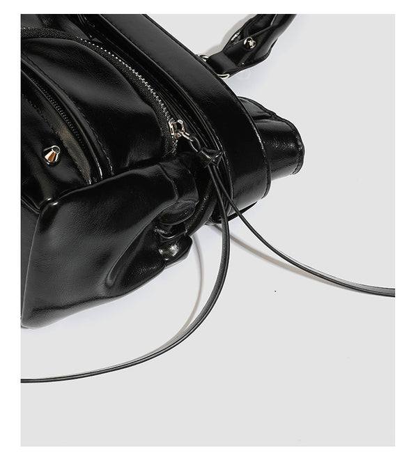 Black glossy structured tote bag with rivet and buckle detail, dual top handles, and detachable shoulder strap, detail view