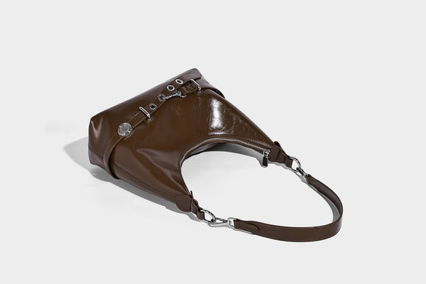 Glossy black slouchy hobo shoulder bag with silver-tone hardware, belt-style grommet strap at base, and long adjustable