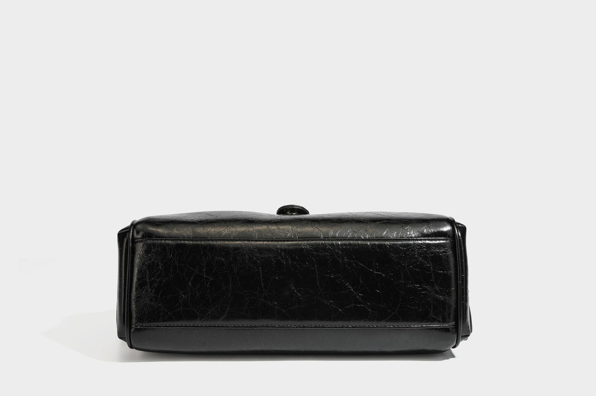 Glänzende, geknautschte Barrel-Satchel mit zwei oberen Tragegriffen, vorderem Klappen-Riemen-Panel, Ring- und Nietenbeschlägen sowie einem abnehmbaren