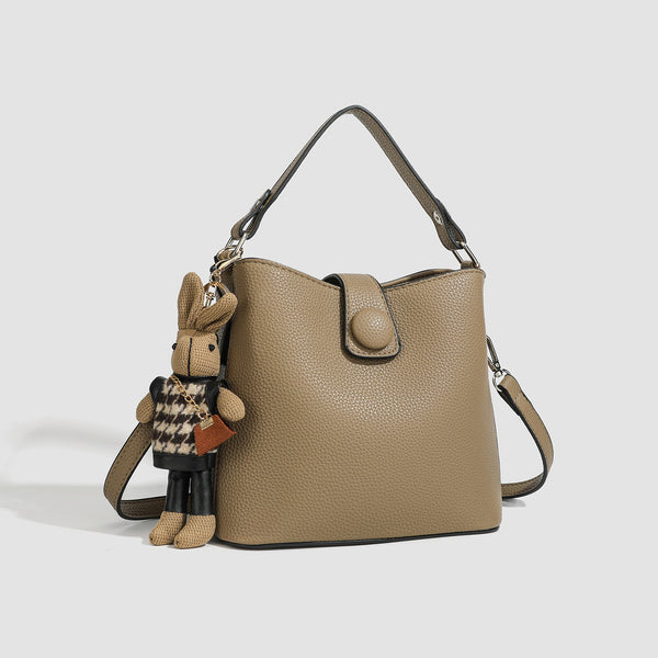 Structured taupe pebbled-texture bucket bag with top handle, silver ring hardware, tab-and-button closure, and knit bunny