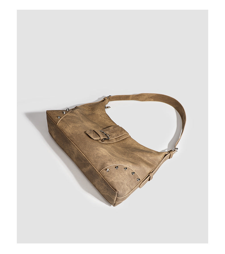 Slouchy trapezoid hobo shoulder bag with distressed textured finish, silver rivet corner accents, centre buckle strap, and