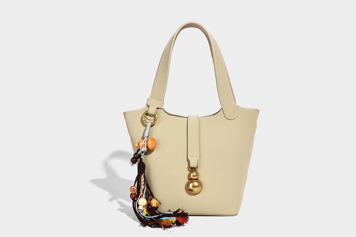 Kleine matte Beuteltasche mit genarbter Oberfläche, antikgoldfarbenen Ringbeschlägen, Perlen- und Quastenanhänger, kurzen Tragegriffen oben und