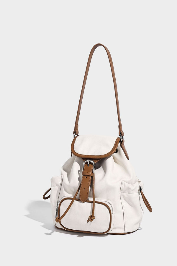 Compact denim drawstring backpack with white leather-look piping, flap-top buckle closure, front zip pocket, and silver-tone
