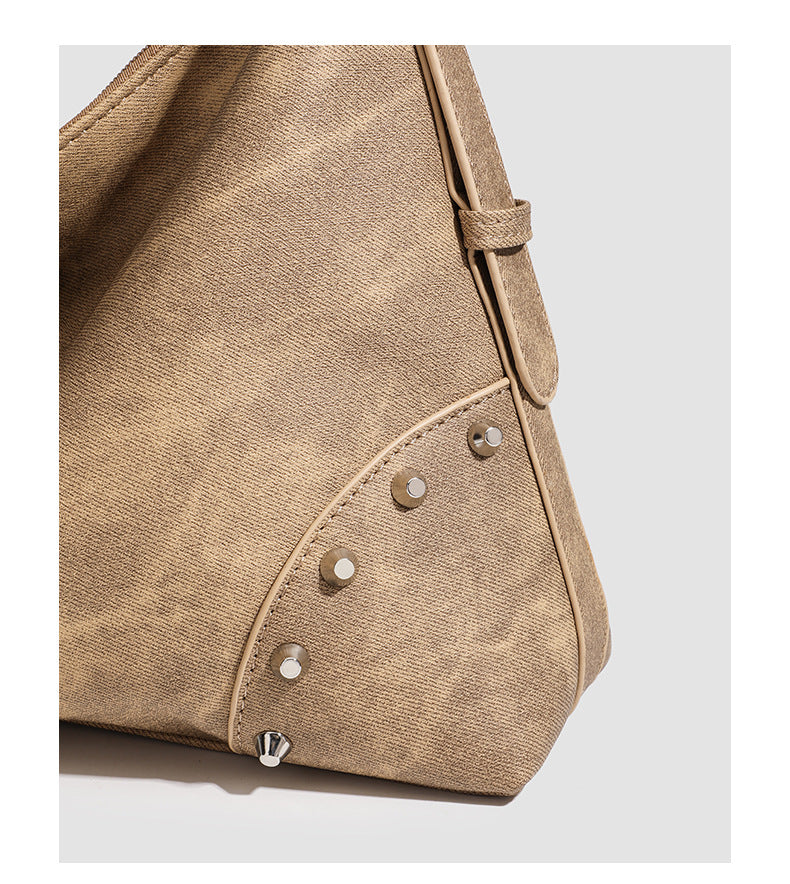 Slouchy trapezoid hobo shoulder bag with distressed textured finish, silver rivet corner accents, centre buckle strap, and