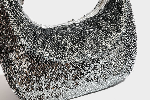 Kleine sichelförmige Schultertasche mit vollständig mit silberfarbenen Pailletten besetzter Außenseite, transparentem Henkel aus kugelförmigen Perlen und Reißverschluss in Silberoptik