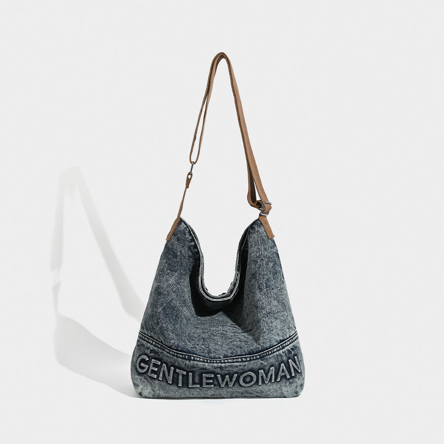 Washed blue denim slouchy open-top shoulder tote bag with tan leather-look adjustable crossbody strap and embroidered, front