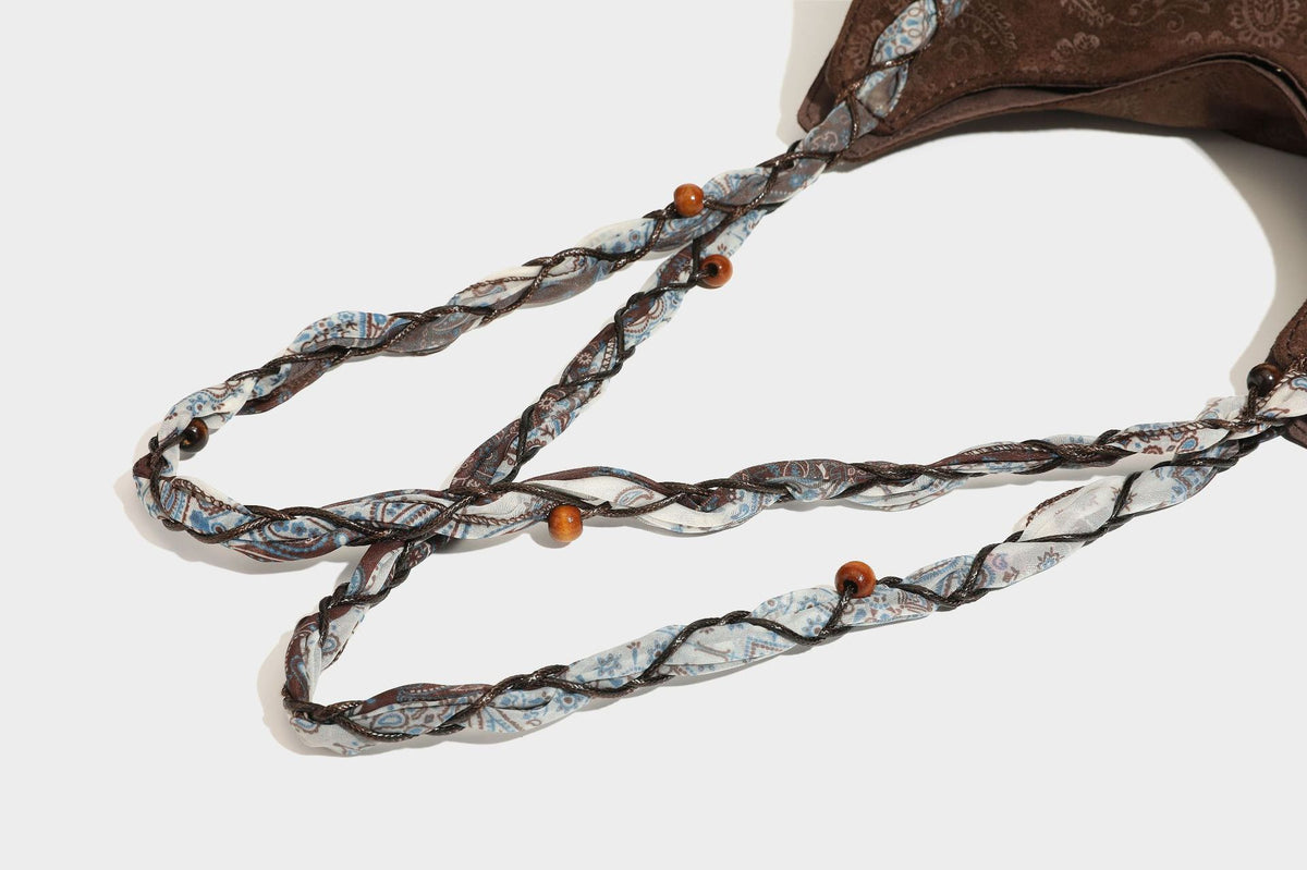 Slouchy paisley-embossed suede-look shoulder tote bag with braided patterned fabric straps and wood bead accents, detail view