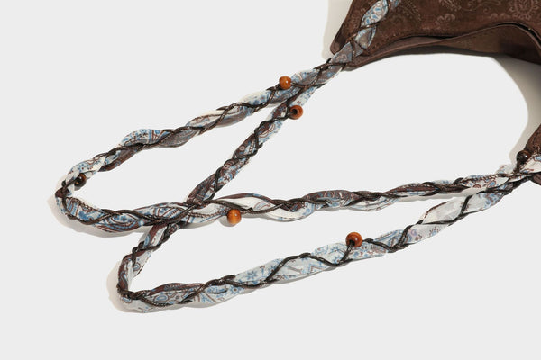 Slouchy paisley-embossed suede-look shoulder tote bag with braided patterned fabric straps and wood bead accents, detail view