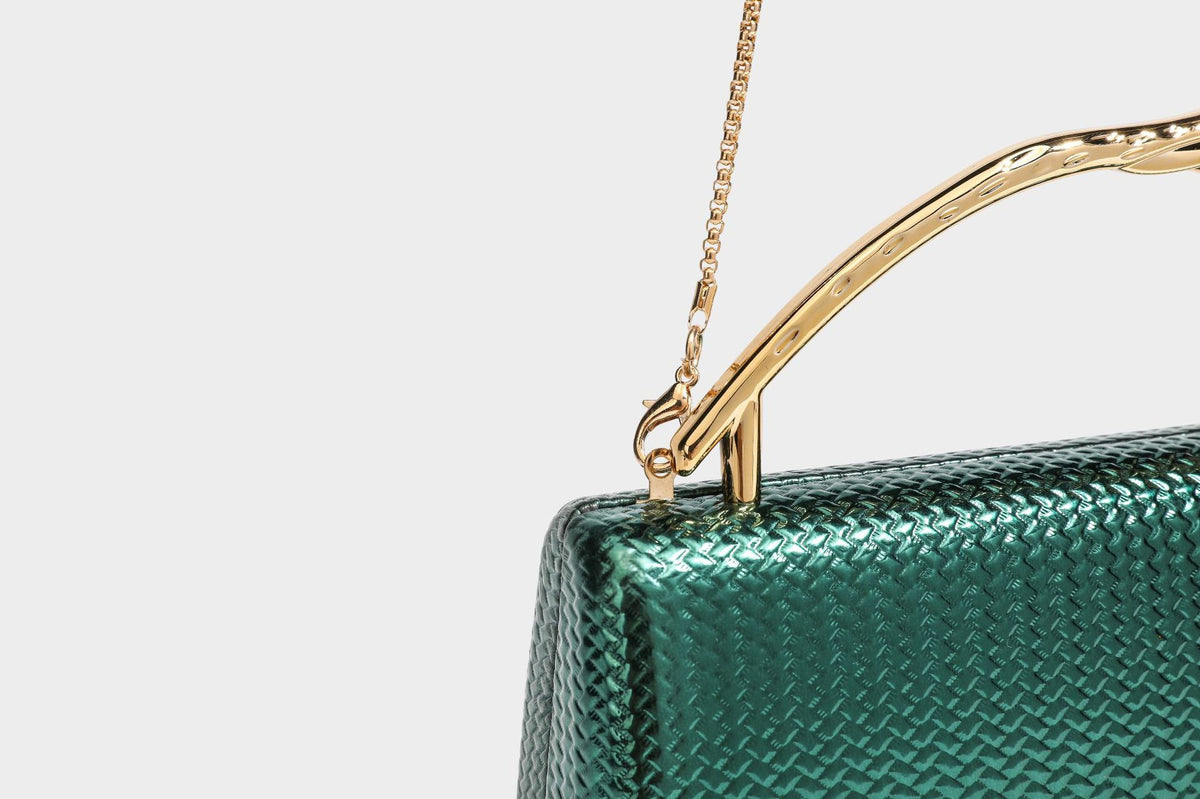 Structured rectangular metallic woven clutch bag with sculptural gold-tone leaf top handle and detachable chain strap, detail