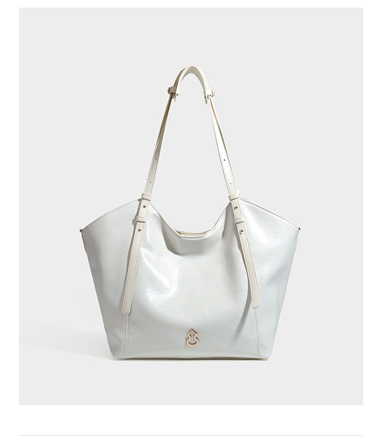 Große, glänzende Tote-Bag aus schwarzem Lederimitat mit geknitterter Optik, lässig fallender Trapezsilhouette, zwei Schulterriemen und goldfarbenen