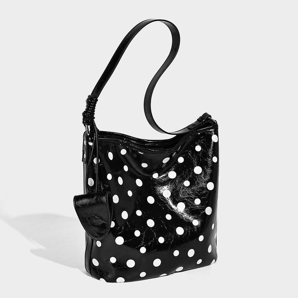 Glänzende schwarze Schultertasche im Bucket-Stil mit weißen Tupfen, langem verstellbarem Riemen und Kordelzugverschluss, Vorderansicht