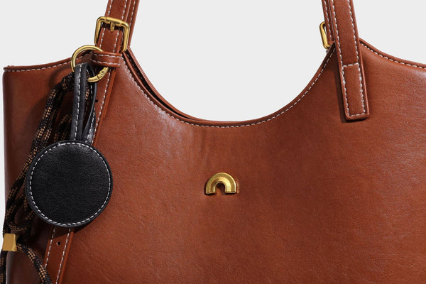 Structured smooth leather-look tote bag with long shoulder strap, gold-tone hardware, and hanging tassel-coin charm, detail