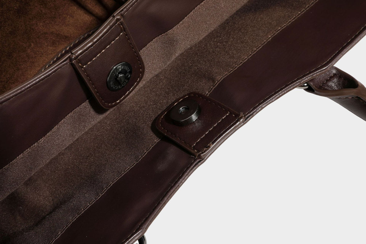 Large structured tote bag with matte suede-like body, smooth leather-look trim, front zip pocket, stud hardware, and