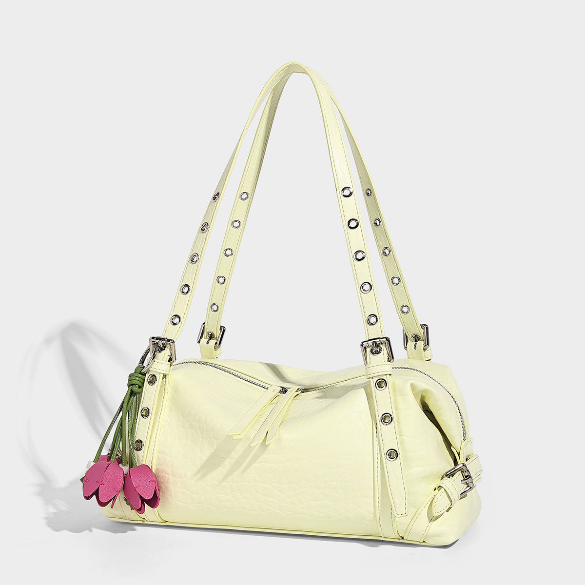 Pale yellow leather-look barrel bag with silver grommet-studded shoulder straps, top zip closure, and pink tulip floral