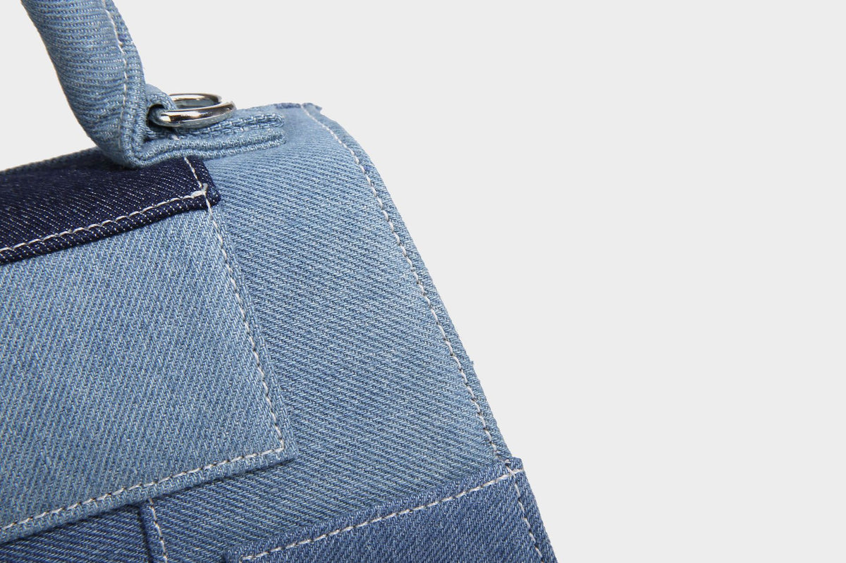 Structured patchwork denim trapezoid satchel bag with frayed panel trim, rounded top handle, and silver-tone hardware, detail